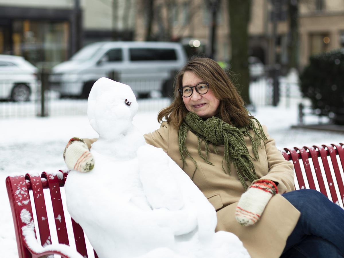 Katri Söder istuu lumisella puiston penkillä vieressään lumiukko.